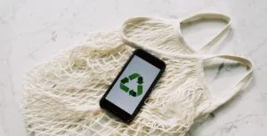 A smartphone showing the recycling symbol, lying on a tote bag