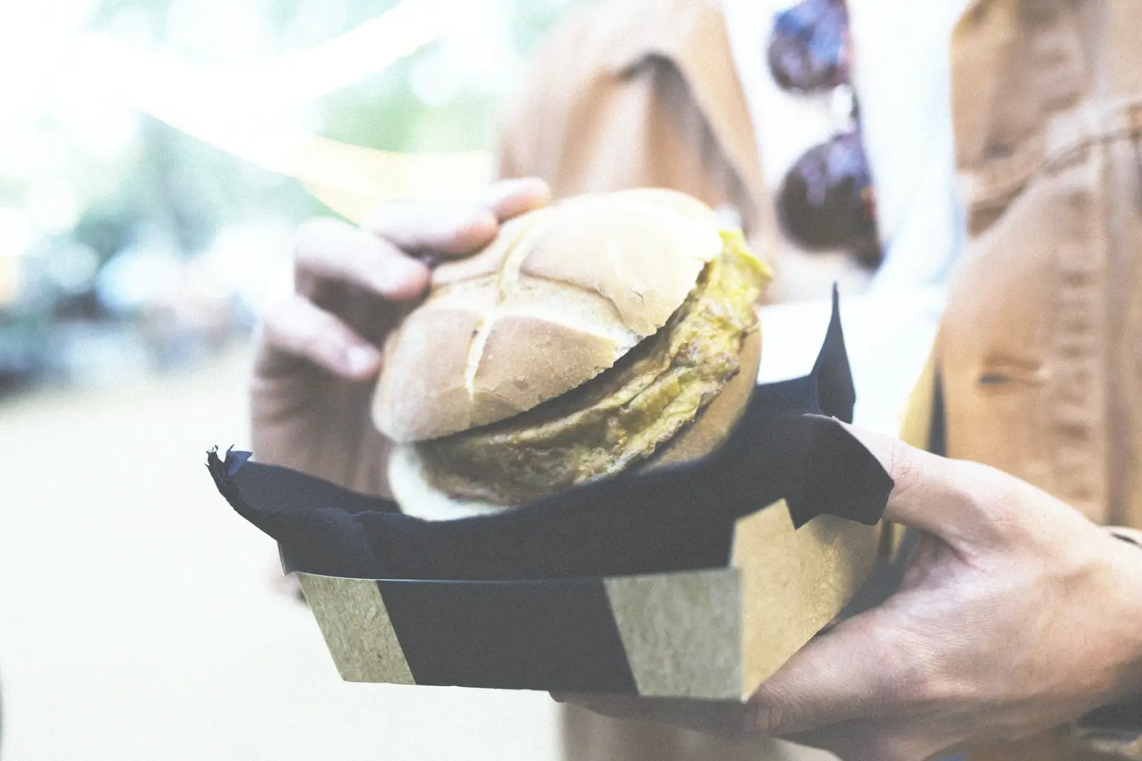 Two hands passing on a burger in a cardboard tray